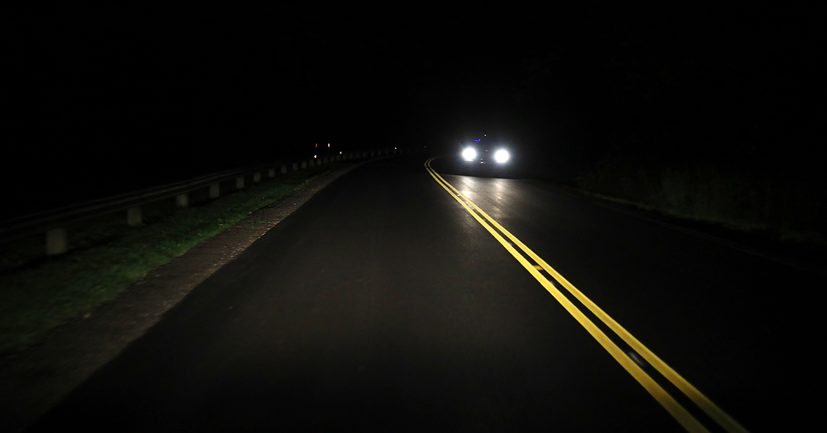 A car with headlights on driving down a road at night